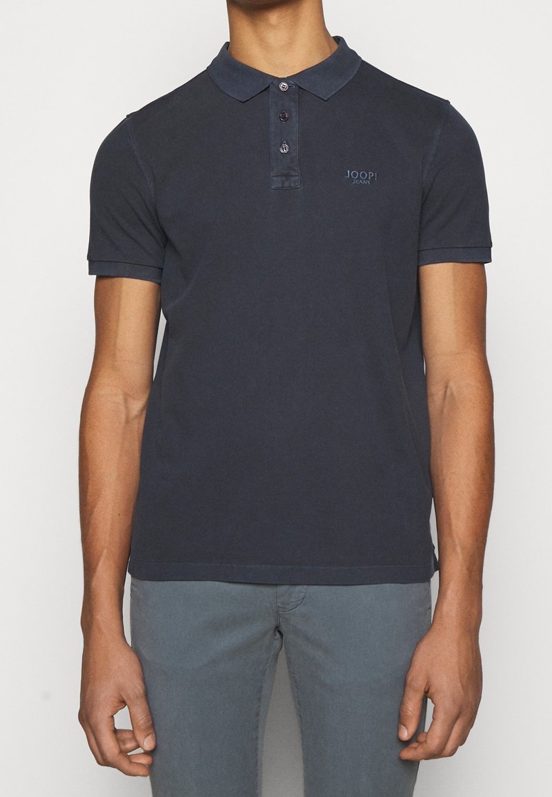 Polo-shirt bleu foncé avec une patte de boutonnage à trois boutons, des manches courtes et un petit logo brodé sur la poitrine gauche. Tissu en coton lisse.