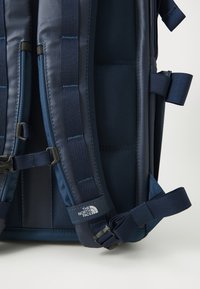 Marineblauer Rucksack mit gepolsterten Mesh-Trägern, strapazierfähigem Stoff, verstellbarem Zubehör und Logo-Akzenten. Bietet ein strukturiertes Design und mehrere Taschen.