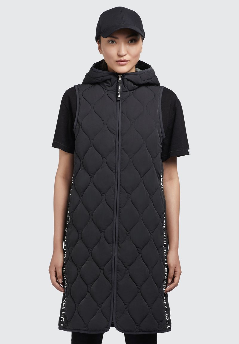 Gilet senza maniche imbottito nero con cappuccio, zip frontale e dettagli testuali verticali sui lati. Texture liscia e design allungato.