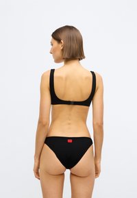 Ensemble bikini noir côtelé comprenant un bralette à bretelles larges avec une fermeture à agrafe et un bas taille basse orné d'un petit logo rouge.