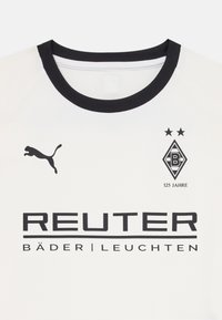 Bijela sportska majica s crnim okruglim izrezom, koja ima crni Puma logo, tekst "REUTER" i oznaku s "125 Jahre" i dvije zvijezde.