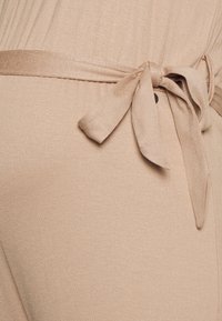 Tecido nu com uma textura suave e lisa, apresentando um detalhe de cinto amarrado na cintura, completando um design ajustado.