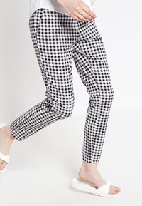 Pantalon à motifs vichy noir et blanc, coupe slim, en coton, avec des poches latérales et une longueur raccourcie, associé à des sandales blanches.