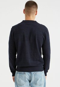 Suéter de punto azul marino hecho de tejido texturizado, con cuello redondo, puños y dobladillo acanalados. Corte ajustado con un acabado suave.