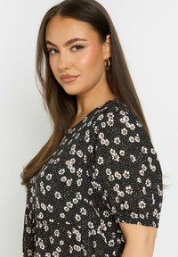 Mustat kukkakuosiset pusero, jossa on pilkkukuosi ja valkoisia sekä oransseja kukkia, lyhyet hihat ja rento malli. Pehmeä kangas.