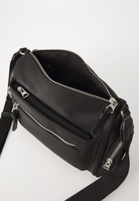 Borsa a tracolla nera con molteplici tasche con zip, realizzata in materiale morbido. Presenta accessori in acciaio inox e una tracolla regolabile.