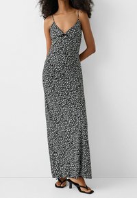 Vestido maxi negro con pequeño patrón floral blanco, tirantes finos, escote en V y silueta ajustada, combinado con sandalias de tacón negras.