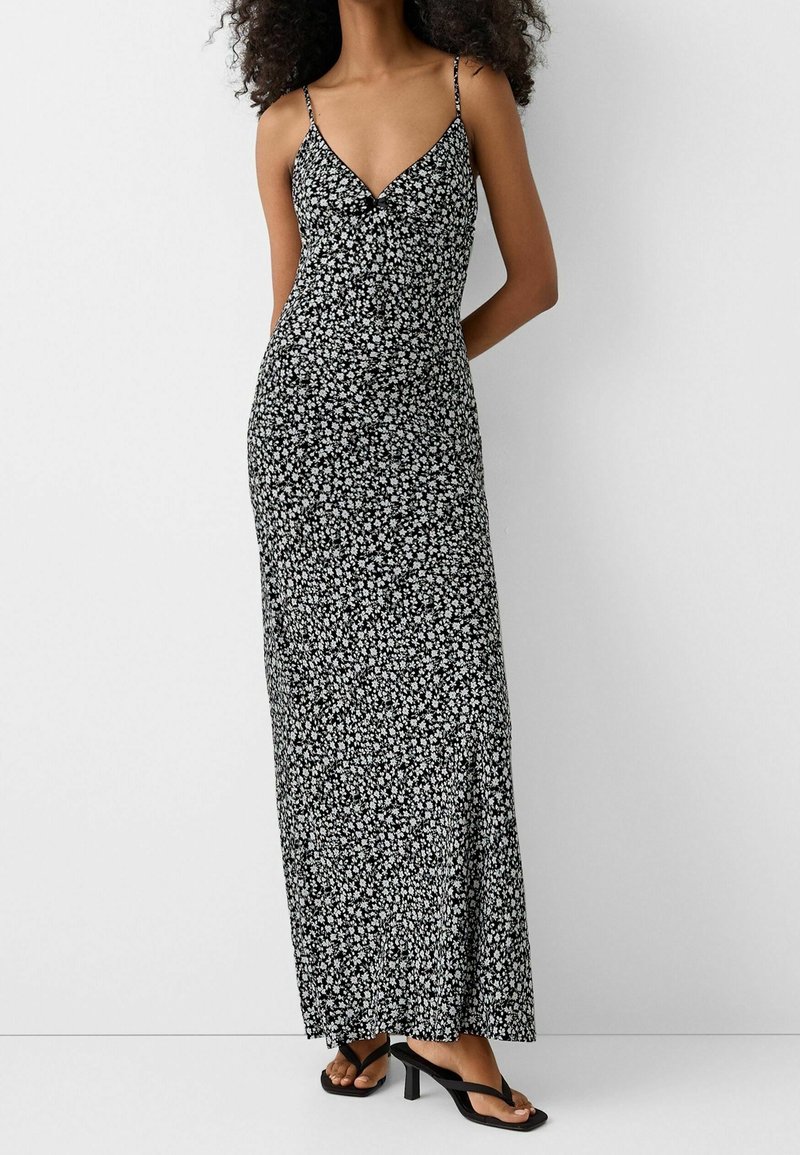 Vestido maxi negro con pequeño patrón floral blanco, tirantes finos, escote en V y silueta ajustada, combinado con sandalias de tacón negras.