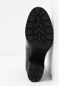 Černá podrážka boty s robustním vzorem, umístěná na bílém pozadí pro zdůraznění jejího designu a textury.