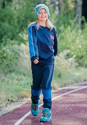 Sininen huppari punaisella logolla, yhteensopivat verkkarit ja turkoosi pipo; siniset ja turkoosit vaelluskengät oransseilla nauhoilla; ulkona radalla.