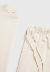Tricou din bumbac bej, cu decolteu rotund și croială lejeră, asortat cu pantaloni de jogger bej, care au un talie elastică și șnur.