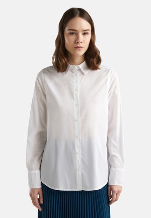 Weißes Langarmhemd mit einem Button-Down-Kragen, glatter Textur und abgerundetem Saum. Kombiniert mit einem plissierten blauen Rock.