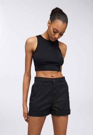 Top corto nero con dettaglio a farfalla, abbinato a pantaloni corti neri con orlo arrotolato in un tessuto liscio. Design semplice e aderente.