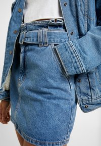 Denim takki nappisulkimella, sininen farkkuhame vyölenkeillä ja vyöllä, hieman kulunut helma, tekstuuripintainen kangas, etupuolen näkymä.