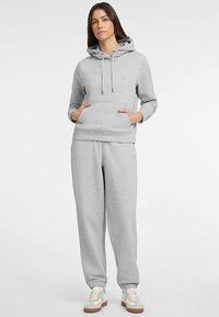 Szara bawełniana bluza z kapturem z przednią kieszenią, regulowanymi sznurkami i prążkowanymi mankietami, w zestawie z dopasowanymi spodniami dresowymi. Oba elementy mają luźny krój.