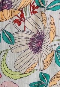 Tissu floral présentant de grandes fleurs contournées en jaune, rose et violet, avec des feuilles vertes et une texture complexe sur un fond clair.