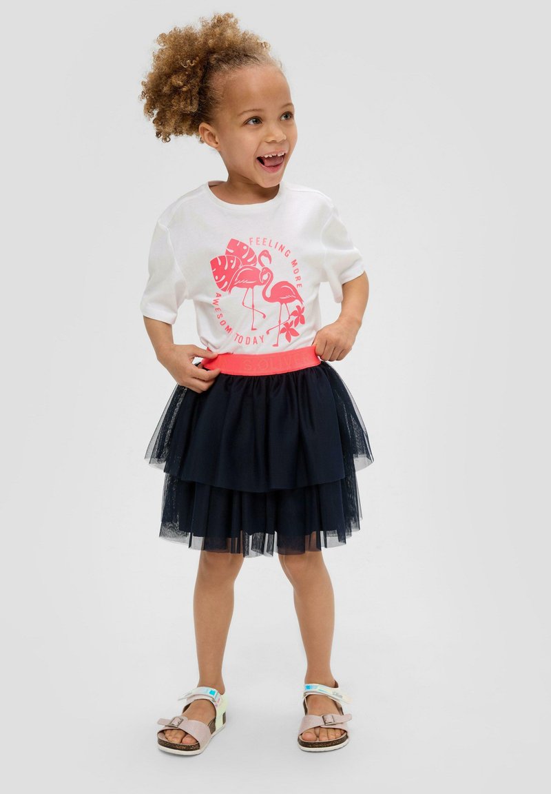 Witte t-shirt met korte mouwen en roze graphic design, gecombineerd met een gelaagde marineblauwe tule rok en multicolore sandalen met verstelbare bandjes.