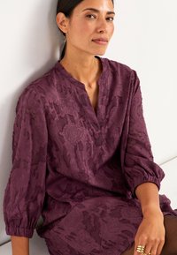 Blomstret bluse i blommefarvet med tekstureret mønster, V-hals og ærmer med tre fjerdedele og elastiske manchetter. Glat, gennemsigtigt stof.