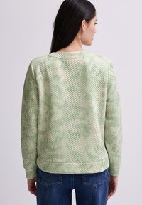 Grön och krämfärgad texturerad sweatshirt med fiskbensmönster, rund halsringning och ribbad midja. Bärs tillsammans med blå denimjeans.