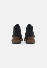 Stivaletti alla caviglia in suede blu navy con dettagli in pelle marrone e suole in gomma texturizzata. Presentano pannelli laterali elastici e un design a punta rotonda.