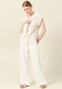 Camicia leggera, con bottoni, a righe verticali pastello, abbinata a pantaloni bianchi svasati e sandali beige; un maglione di lana gettato sulle spalle.