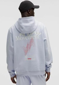 Lyseblå hoodie med stor grafisk tekst "MINDFUL Movement" på ryggen, der har røde bølgemønstre og hvide detaljer. Hættedesign.