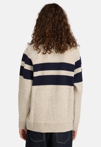 Beżowy sweter dziany w granatowe poziome pasy, z luźnym krojem, ściągaczami przy mankietach oraz miękką fakturą.