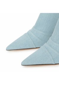 Decolletés a punta in denim blu chiaro con dettagli cuciti. La silhouette snella e il tessuto testurizzato creano un aspetto elegante.