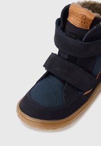 Scarpa blu navy realizzata in suede e tessuto a rete, dotata di una fascia in velcro, dettagli in pelle marrone e una suola in gomma testurizzata.