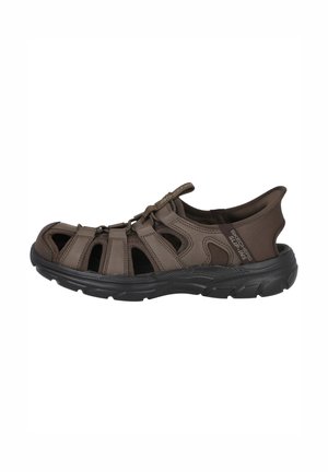 Sandaña marrón con diseño abierto, que presenta un upper texturizado, cierre elástico tipo bungee y una suela de goma negra resistente.
