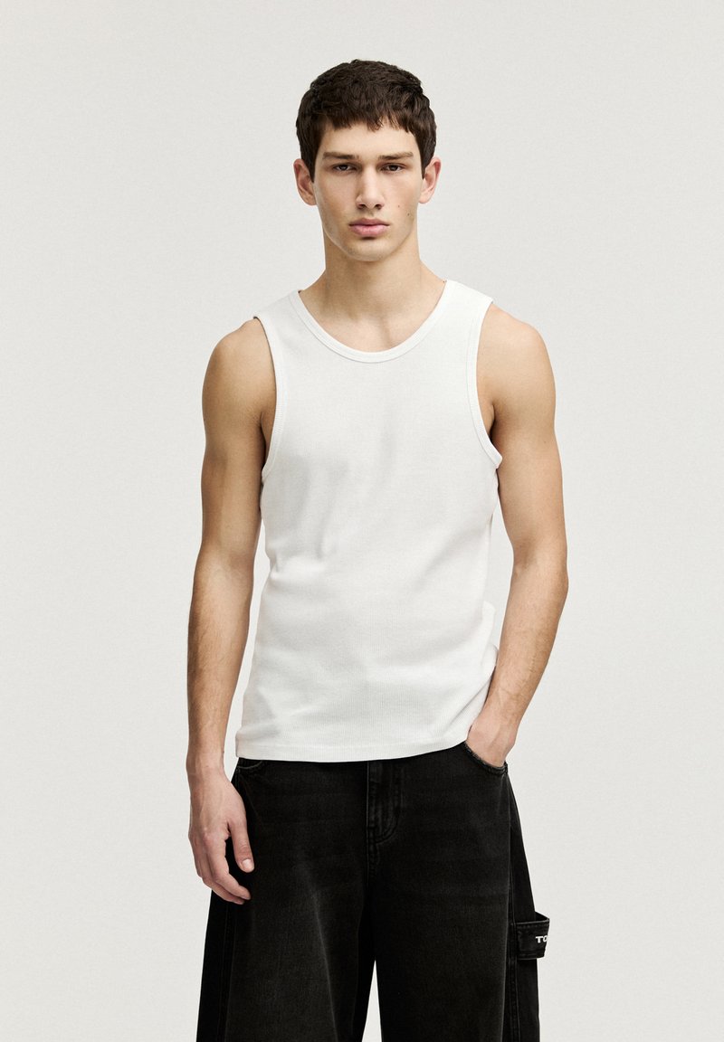 Débardeur blanc côtelé avec un col rond, associé à un short en denim noir ample avec poches latérales et une branding subtile.