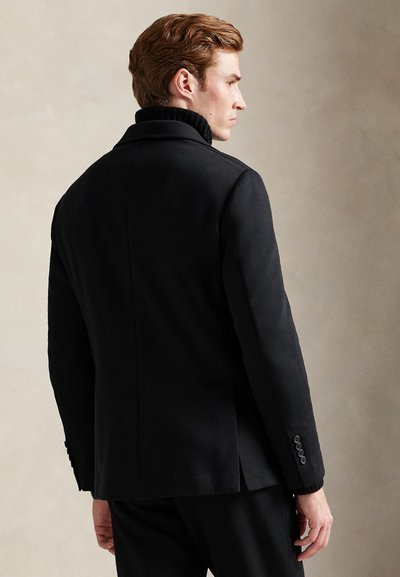 Μαύρο ραμμένο παλτό με ψηλό γιακά, ομαλή υφή και μανσέτες με κουμπιά. Διαθέτει κομψό σχεδιασμό και εφαρμοστή γραμμή.