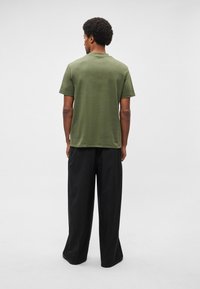 Oļveļzaļa īsroku krekls ar apaļu kakla izgriezumu, kombinēts ar vaļīgām melnām biksēm. Teksturēts audums ar gludu virsmu.