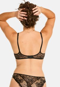 Soutien-gorge en dentelle noire avec des bretelles réglables et une fermeture à crochets au dos. Des détails floraux délicats soulignent le design raffiné. Culotte en dentelle assortie.