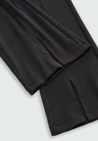 Pantalons en tissu côtelé noir avec une coupe ajustée, des détails de couture prononcés et des fentes sur les côtés près de l'ourlet pour un style supplémentaire.