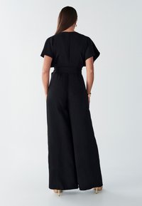 Czarny kombinezon z krótkimi rękawami, taliowany w pasie i szerokimi nogawkami. Miękki materiał o gładkiej fakturze z zamkiem z tyłu.