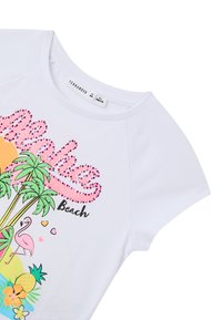 T-shirt bianco a maniche corte con grafiche colorate a tema spiaggia, tra cui palme, un fenicottero e lettering rosa scintillante "Aloha".