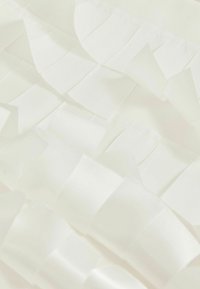 Valge kangas, millel on tekstureeritud volangid ja läikiv, siledam viimistlus. Materjal on kerge ja omab kihilist, dimensioonilist välimust.