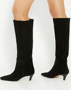 Bottes noires en suède montant jusqu'au genou, à bout pointu et petit talon empilé, avec une texture lisse et une silhouette propre et élégante.