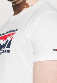Hvid bomulds T-shirt med et farverigt grafisk design, tekst "New York City" og små logo detaljer på ærmet. Rund halsudskæring, korte ærmer.