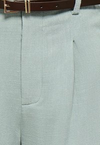 Pantalon gris clair texturé avec une ceinture en cuir noir passée dans les passants.