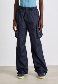 Personne portant un pantalon cargo ample bleu marine avec plusieurs poches et des baskets bleu marine avec des semelles claires.