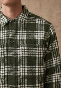 Groen-wit geruit flanellen overhemd met kraag, voorzien van een knoopsluiting aan de voorkant, borstzak en een gestructureerd stofpatroon.