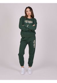 Groene sweatshirt en bijpassende joggers met bedrukte tekst. Gemaakt van zachte stof, met een ronde halslijn en elastische manchetten. Witte sneakers.