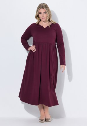 Bordeaux lange mouw jurk met V-hals, geraffineerde taille, vloeiende rok en gladde textuur. Gecombineerd met zilveren ballerina's.