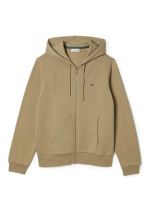 Sweat à capuche beige zippé avec poches avant, capuche réglable avec cordon de serrage et petit logo crocodile vert sur la poitrine gauche.