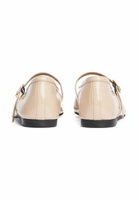 Scarpe in pelle verniciata beige con punta arrotondata e tacco basso, dotate di una fascia laterale con una fibbia dorata e dettagli neri.