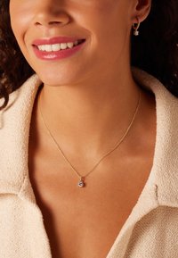 Collar de cadena de oro con un colgante de piedra preciosa clara y redonda. Los pendientes a juego cuentan con una pequeña piedra, engastada en un diseño de aro dorado.