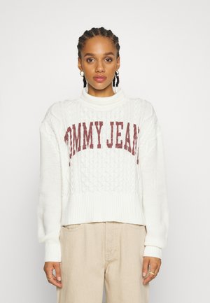 Baltas megztinis su tekstūriniu raštu ir aukšta apykakle, ant krūtinės puikuojasi ryškus bordo spalvos "TOMMY JEANS" logotipas.