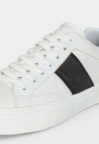 Λευκό sneaker χαμηλής κοπής με λευκά κορδόνια, υφασμάτινη μαύρη πλευρική λωρίδα με διακριτικό μοτίβο λογότυπου και λευκή εύκαμπτη σόλα.